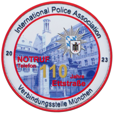 Rundes Emblem der International Police Association mit Jahreszahlen und Münchener Skyline.