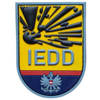 Wappen der IEDD mit Explosionseffekt und Adler im unteren Bereich.