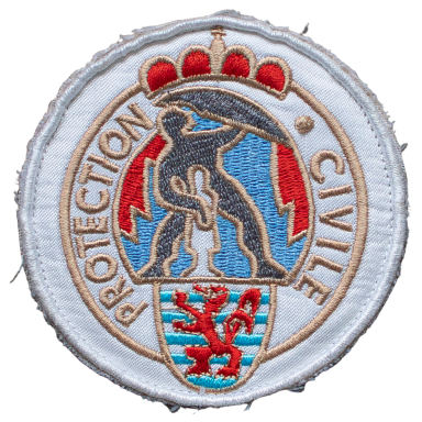 Abzeichen der Protection Civile mit Ornamenten und einer Figur, die eine Rettungsaktion symbolisiert.